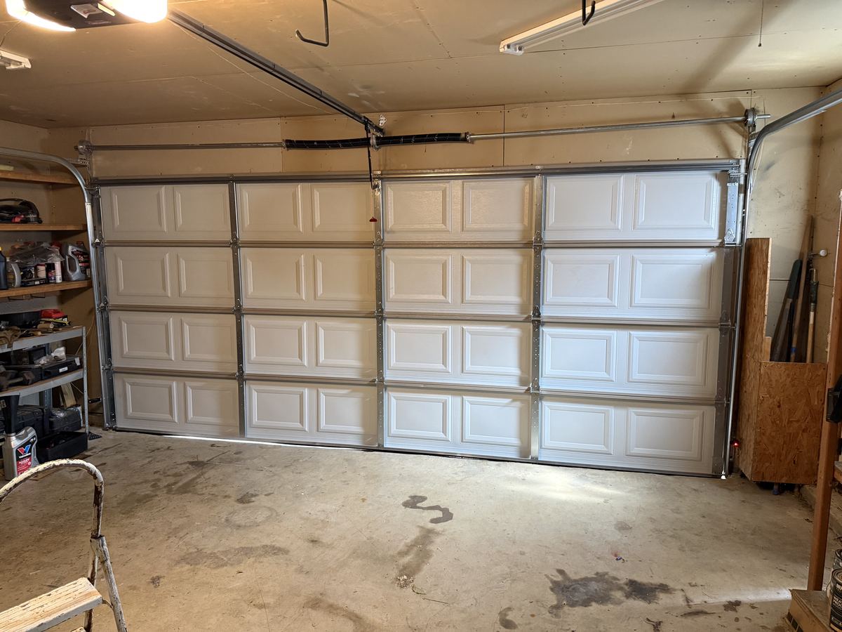 Inside view of a white raised-panel garage door with the torsion spring mounted above the opening